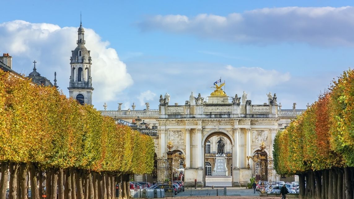Ville de Nancy. Des arbres sont alignés à gauche et à droite pour créer une allée jusqu'à un monument.