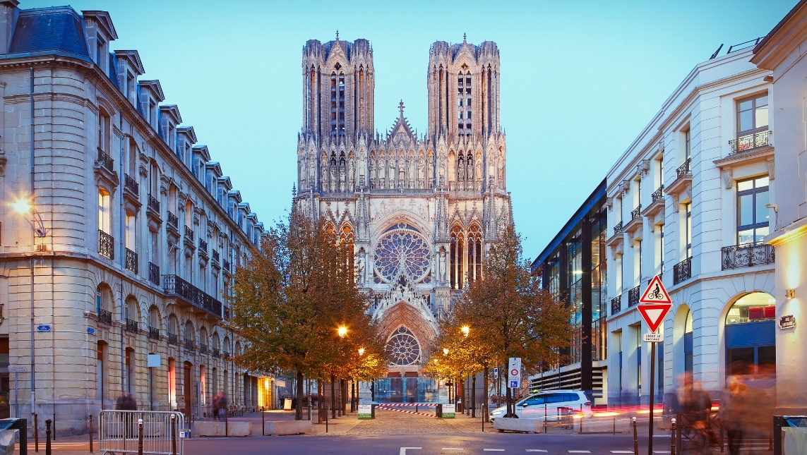 Ville de Reims. Cathédrale aperçu au loin devant une allée. Des immeubles sur chaque côté de l'allée.