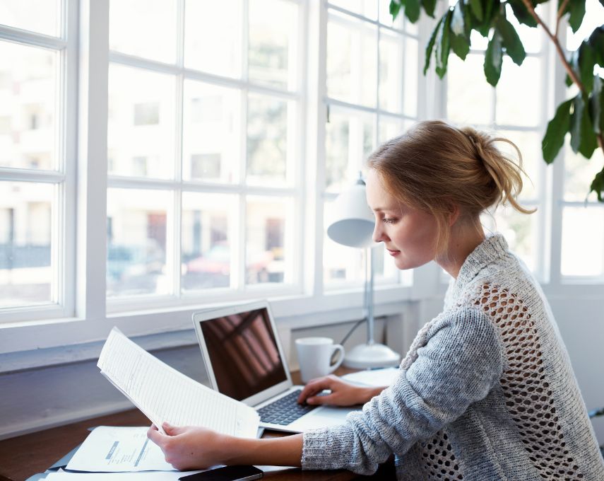 Femme travaillant sur un ordinateur portable et consultant des documents à son bureau.