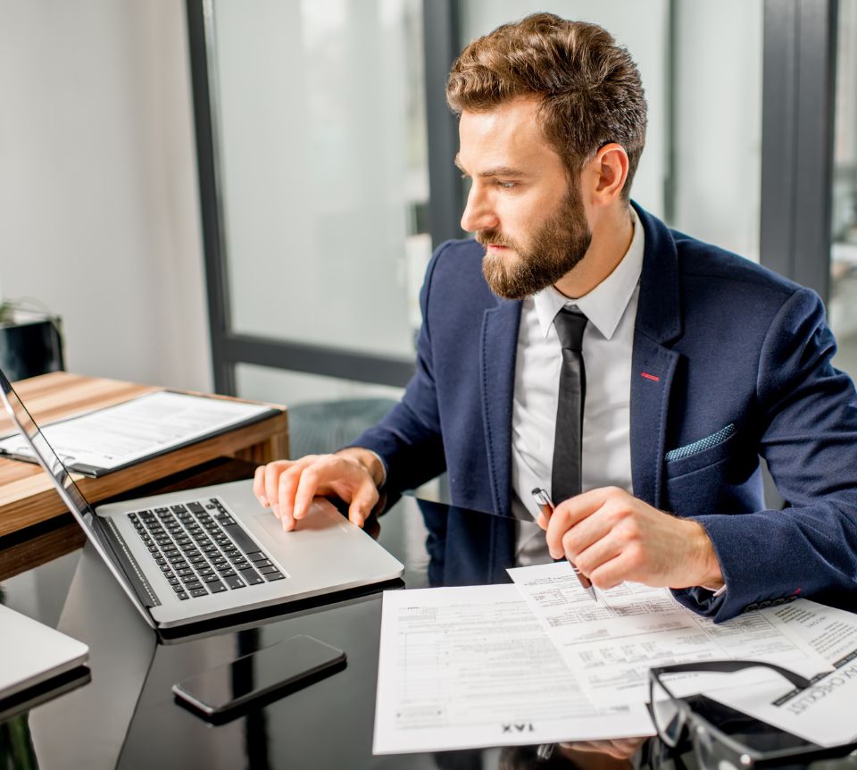 Professionnel en costume consultant des documents sur son ordinateur portable, dans un bureau.