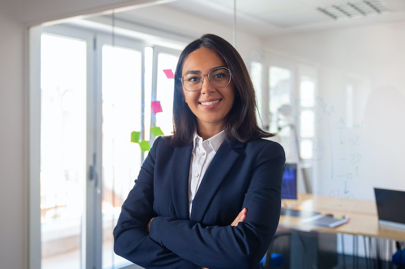 confident-latin-business-leader-portrait-young-businesswoman-in-suit-and-glasses-posing-with-arms-folded-looking-at-camera-and-smiling-female-leadership-concept