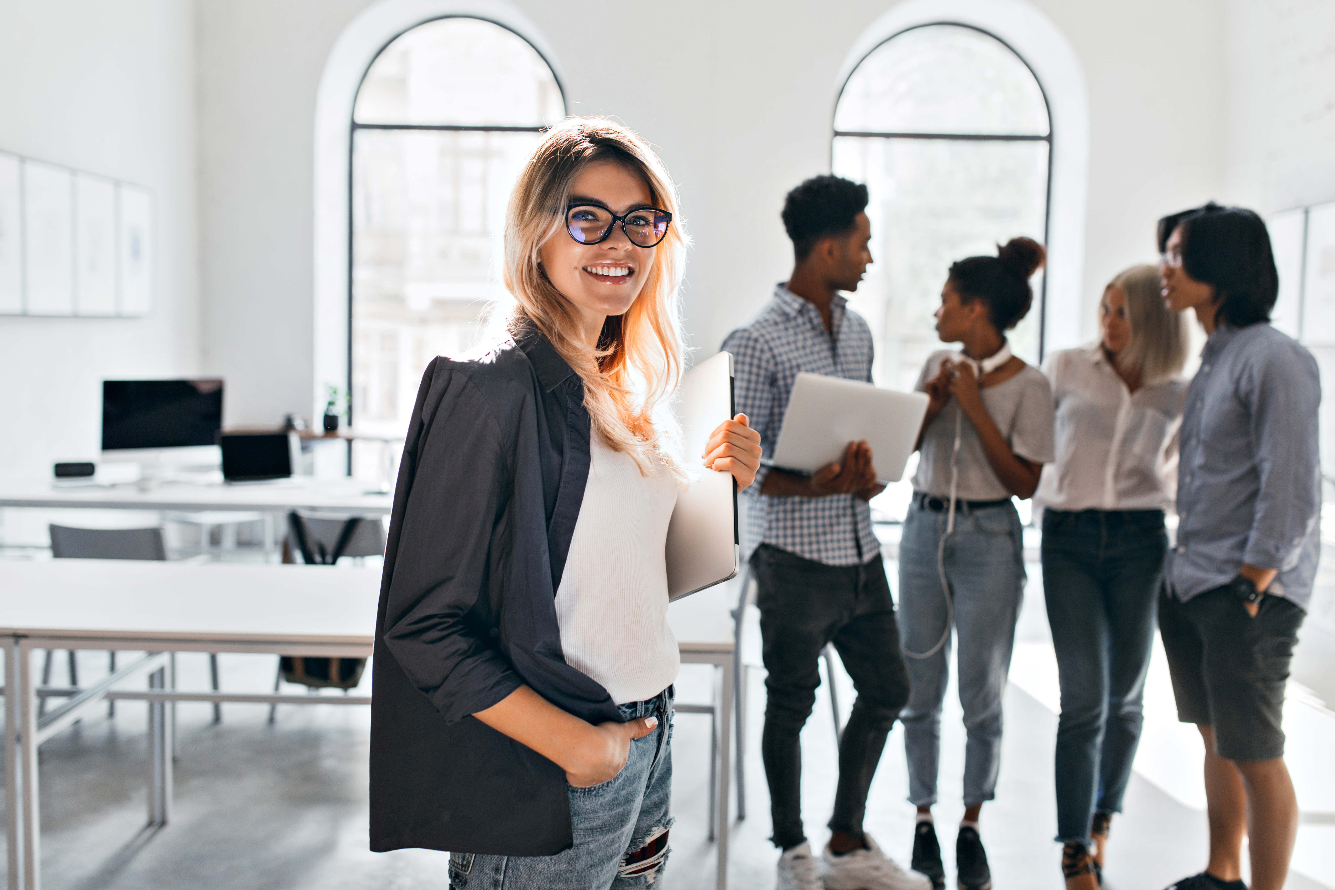 indoor-portrait-of-elegant-business-lady-in-black-jacket-and-her-team-african-office-manager-in-white-sneakers-carrying-laptop-and-talking-with-mulatto-woman-in-jeans